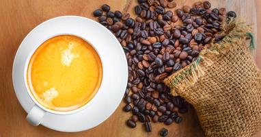 Top view of coffee cup has golden foam and mixed or blend coffee beans in a brown sack on wooden backgrou photo