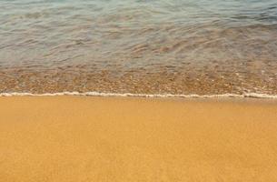 Background with golden sand on the coast of the island of Crete. Abstract surface with sand and clear sea water for text. photo