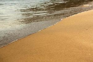 Background with golden sand on the coast of the island of Crete. Abstract surface with sand and clear sea water for text. photo