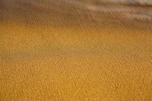 Background with golden sand on the coast of the island of Crete. Abstract surface with sand and clear sea water for text. photo