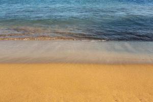 Background with golden sand on the coast of the island of Crete. Abstract surface with sand and clear sea water for text. photo