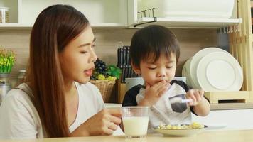 contento asiatico madre e figlio a casa su vacanza. ragazzo mangiare prima colazione e potabile latte video