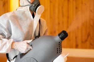 un técnico profesional con traje de prevención rocía una solución esterilizante con una máquina de pulverización eléctrica en el suelo de madera y fondo blanco con luz de estudio. foto