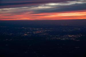 el crepúsculo de la noche desde el avión a reacción ve el cielo azul naranja rojo con la luz de la ciudad de Tailandia debajo foto