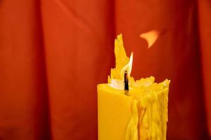 cerca de la vela amarilla fundida y la llama del fuego con el fondo de la cortina roja. foto