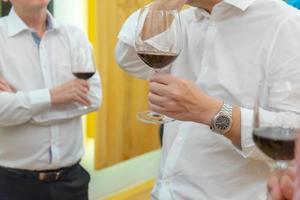 cerca de las manos de dos hombres de negocios de camisa blanca que sostienen una copa de vino, hablan y negocian en asuntos políticos y de negocios en la cena. foto