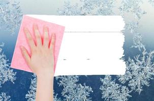 hand deletes winter snowflake on window by rag photo