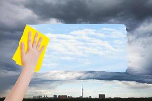 hand deletes rainy cloud over city by yellow cloth photo