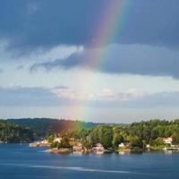 green coast with village and rainbow in blue sky photo