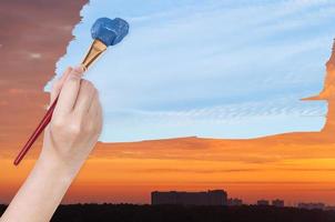 paintbrush paints blue day sky on orange sunset photo