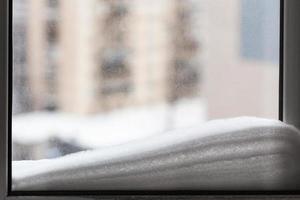 snow on window pane and houses on background photo