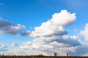 large cumulus clouds in sky over houses and forest photo