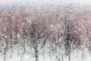 gotas de agua de la nieve derretida en el vidrio de la ventana de la casa foto