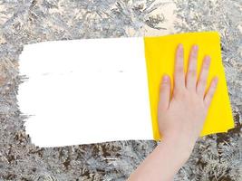 la mano elimina el patrón congelado en el vidrio con un trapo amarillo foto