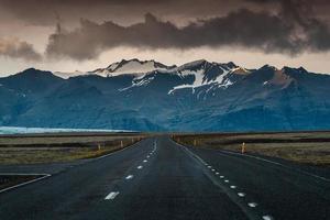 Carretera asfaltada recta con tormenta sobre la montaña en un día sombrío en Islandia foto