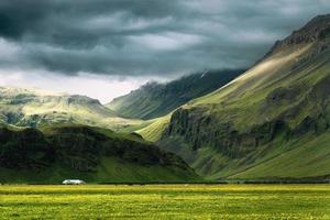 Dramatic Icelandic mountain with sunlight shining through storm clouds and house on field in summer at Iceland photo