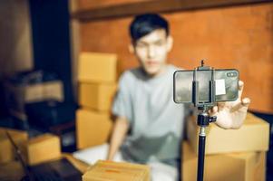 An Asian man uses a mobile phone to take orders and display items in a box that records live streaming video online at the store. small business owner Asian online market delivery concept photo
