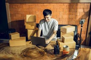 un hombre asiático usa un teléfono móvil para tomar pedidos y mostrar artículos en una caja que graba video en vivo en línea en la tienda. concepto de entrega de mercado en línea asiático propietario de pequeña empresa foto