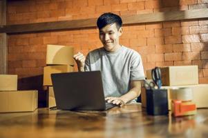 An Asian man uses a mobile phone to take orders and display items in a box that records live streaming video online at the store. small business owner Asian online market delivery concept photo