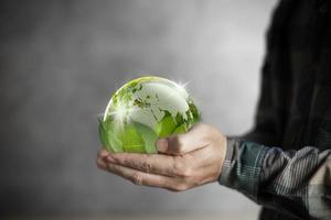 mano humana del día de la tierra sosteniendo un mundo verde respaldado por hojas, conservación y concepto ambiental. foto