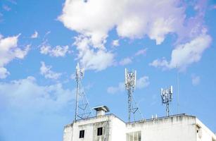 torre de comunicación con antenas en la parte superior del edificio y cielo azul brillante con fondo de nubes.