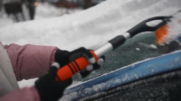 Junge Frau in rosa Puffmantel bürstet Schnee vom Auto video