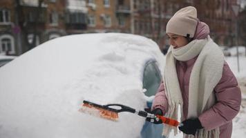 mujer joven en abrigo rosa hinchado cepilla la nieve del coche video