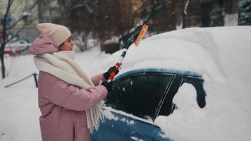 jong vrouw in roze gezwollen jas borstels sneeuw uit auto video