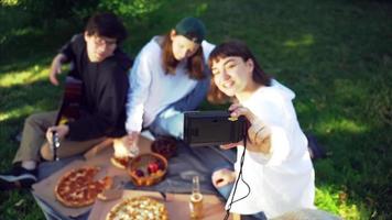 des amis se tiennent ensemble dans un parc en train de manger de la pizza et de la bière prennent un selfie avec un appareil photo video