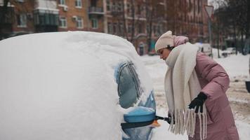 Young woman in pink puffy coat brushes snow off car video