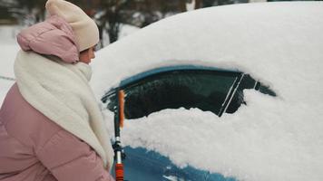 mujer joven en abrigo rosa hinchado cepilla la nieve del coche video