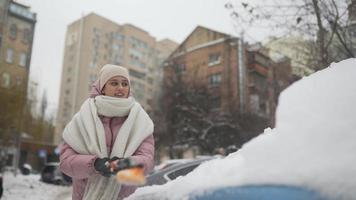 Young woman in pink puffy coat brushes snow off car video