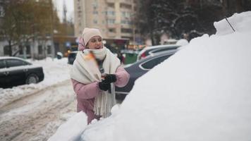 giovane donna nel rosa gonfio cappotto spazzole neve via auto video
