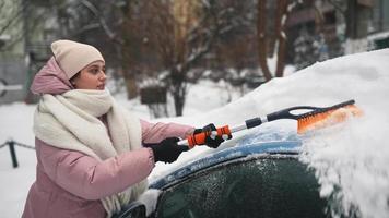 Junge Frau in rosa Puffmantel bürstet Schnee vom Auto video