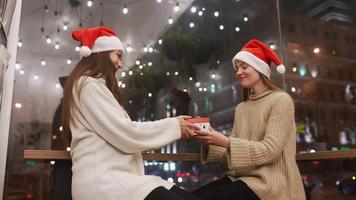 deux jeunes femmes en chapeaux de père noël échangent des cadeaux avec des sourires et des câlins video