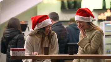 Women friends laugh together telling stories wearing Santa hats in a cafe at night