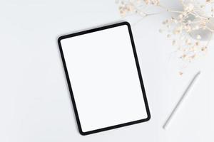 white tablet and stylus with copy space blank screen, light background with dry flower blossoms in vase, top view photo