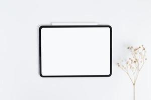 white tablet and stylus with copy space blank screen, light background with dry flower blossoms in vase, top view photo