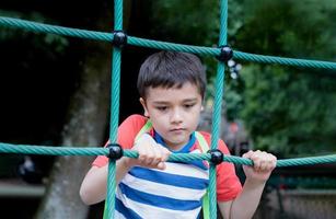 Portrait Kid holding robe in outdoors playground, Child climbing adventure park on sunny day  Spring or sSmmer, Lonely young boy playing alone in public playground. photo