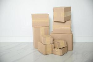 pila de cajas de cartón para mudanzas, habitación vacía con una pared blanca y cajas de cartón con código de barras sin marca en el suelo. entrega de mercancías, compras. cajas de cartón sobre fondo de pared gris. foto