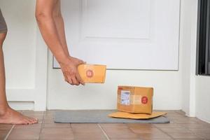 la mujer recoge el paquete en la puerta. caja cerca de la puerta en el piso. Compras en línea, cajas entregadas en la puerta de tu casa. fácil de robar cuando no hay nadie en casa. paquete en caja de cartón en la puerta. servicio de entrega foto