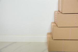 pila de cajas de cartón para mudanzas, habitación vacía con una pared blanca y cajas de cartón con código de barras sin marca en el suelo. entrega de mercancías, compras. cajas de cartón sobre fondo de pared gris. foto