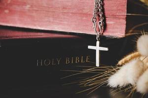 Holy bible book with cross or crucifix on old black wooden background. Christian catholic with protestant pray and study in church. Concept of cognition about faith god and religion, jesus spiritual. photo