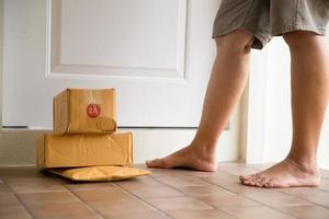 la mujer recoge el paquete en la puerta. caja cerca de la puerta en el piso. Compras en línea, cajas entregadas en la puerta de tu casa. fácil de robar cuando no hay nadie en casa. paquete en caja de cartón en la puerta. servicio de entrega foto