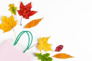 concepto de venta de otoño. pancarta de descuento bolsa de papel y coloridas hojas caídas sobre fondo blanco. foto
