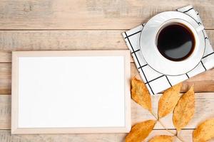 Autumn flat lay. Cup of hot espresso coffee and fallen yellow leaves on wooden background. Empty frame mock up for text. Morning concept. photo