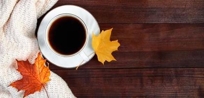 taza de café espresso caliente y hojas amarillas caídas sobre fondo de madera. concepto de mañana de otoño. foto