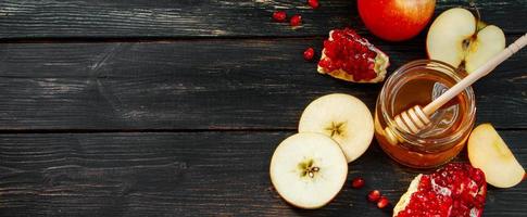 Rosh Hashanah celebration. Jar with honey, apples and pomegranates on dark wooden background. Jewish traditional religious holiday. Place for your text, banner format. photo