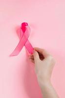 Breast Cancer Awareness Month. Woman's hand holds pink ribbon. Health care concept, cancer control symbol. photo