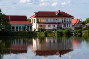 A modern two-storey house with a red tiled roof on the shore of a lake with a reflection in the water. photo